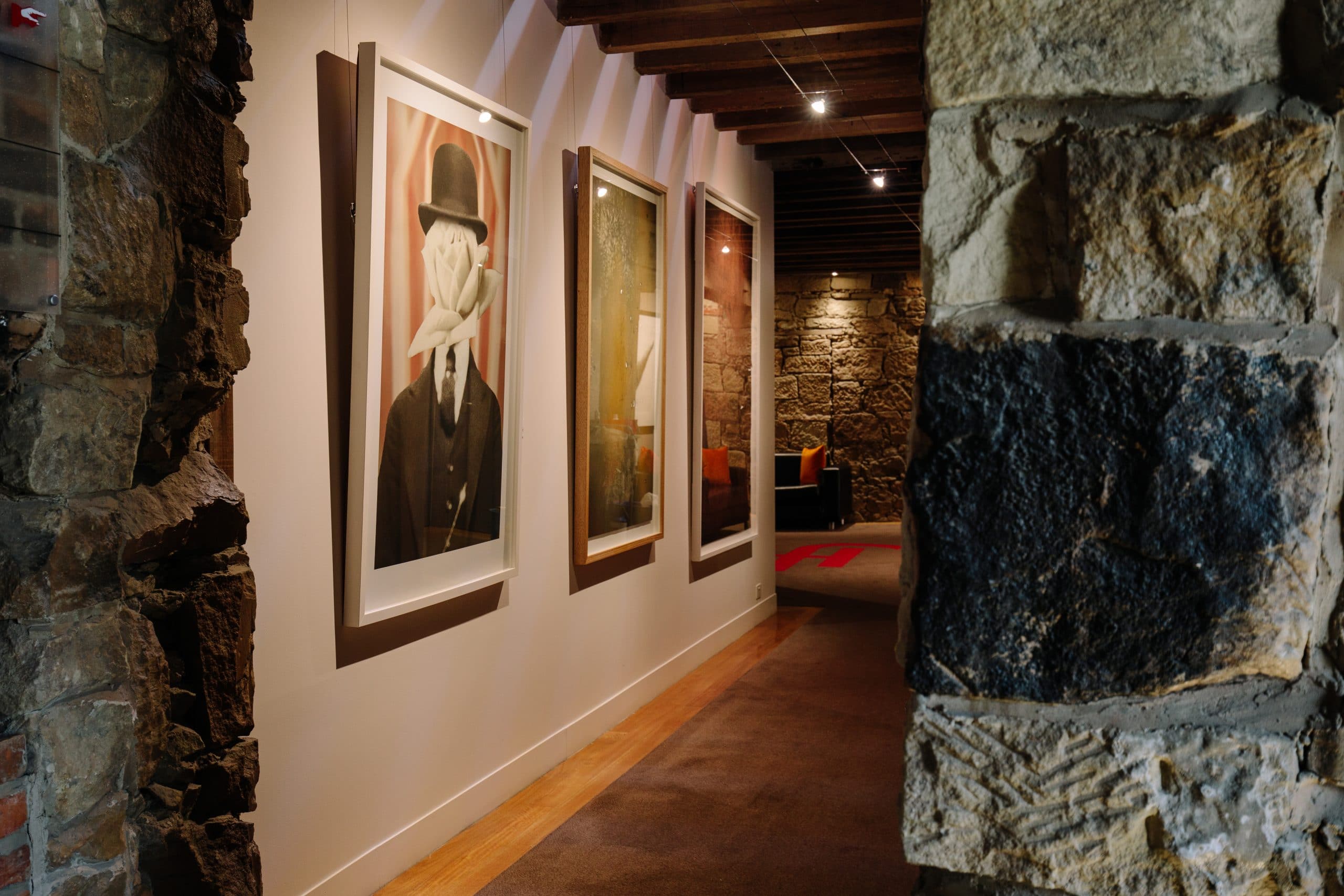 A stone-walled hallway inside Henry Jones Art Hotel in Hobart with paintings hanging on the wall.
