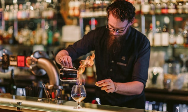 A bartender at IXL Long Bar at the Henry Jones Art Hotel, skillfully preparing a drink at a bar counter, showcasing his skill and attention to detail.